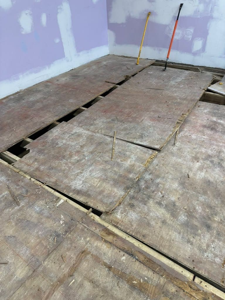 Damaged subfloor panels across a large room before replacement