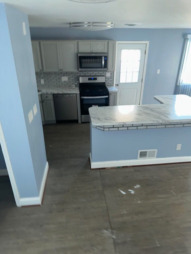 Renovated open kitchen with gray cabinets, stainless appliances, marble-look island, and new plank flooring